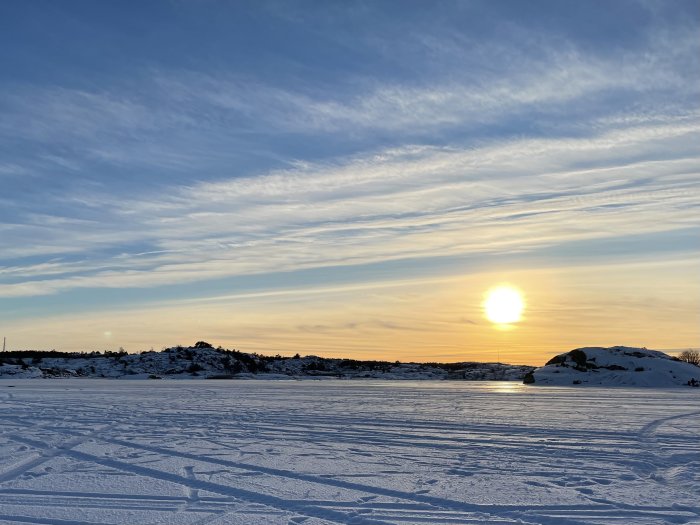 Solnedgång över ett snötäckt landskap med is och bilspår som leder till fasta bilar.