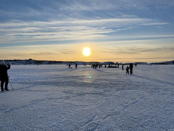 Solnedgång över en isbelagd sjö med människor och två bilar som har kört fast.