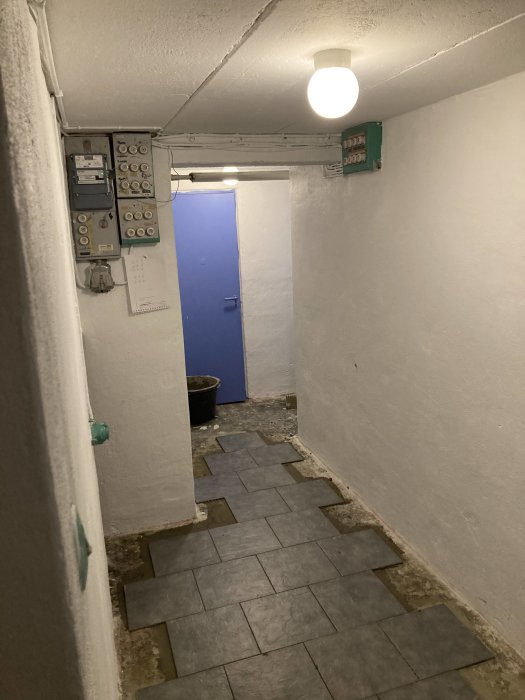 Renoverad källarkorridor med nylagda klinkers och nymålade vita väggar, elcentral på väggen.