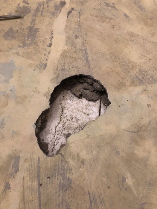 Hål i betonggolv där det syns spruckna kanter och isolering under plattan.