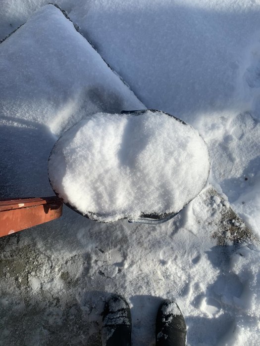 Täckt i snö, en fryst vattenledning syns vid marken med någons fötter i förgrunden.