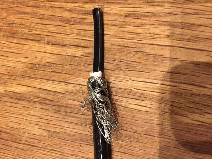 Skalad Raychem kabel med synliga ledningstrådar på träbakgrund.