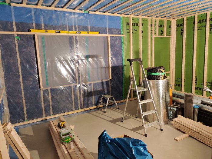 Delvis byggd vägg med isolering och stående installationsskikt, nivåbubbla och stege på arbetsplats.