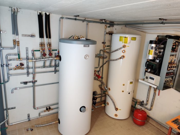 Installation av värmeanläggning med flera varmvattenberedare och en blandning av koppar- och stålrör i ett teknikrum.