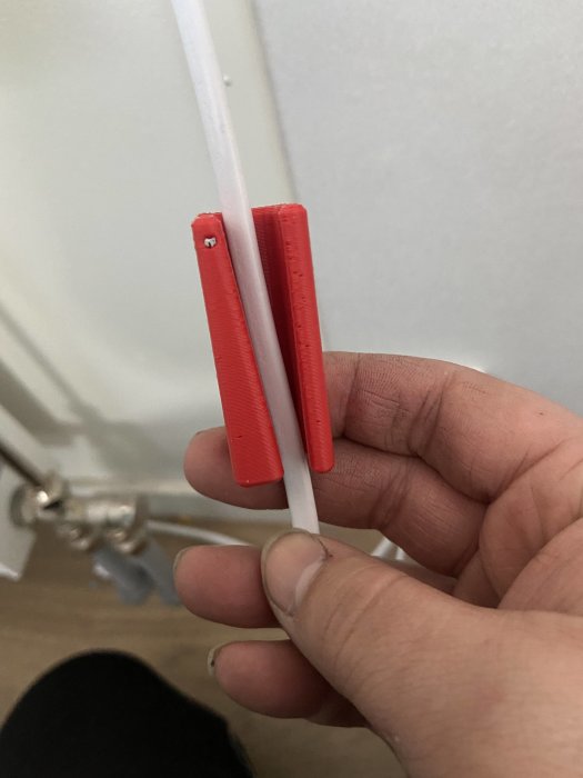 Hand håller en röd 3D-utskriven spiraliseringsprototyp bredvid ogjord kabel.