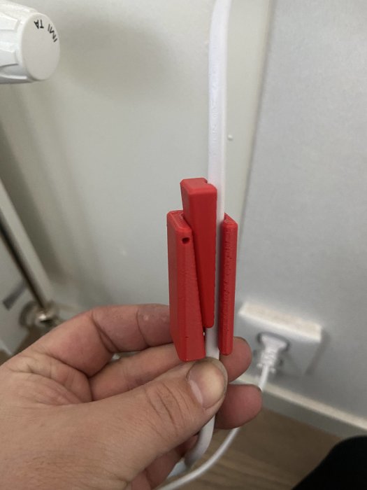 Hand håller en röd plastdel för spiralisering av kabel mot en vägguttag.