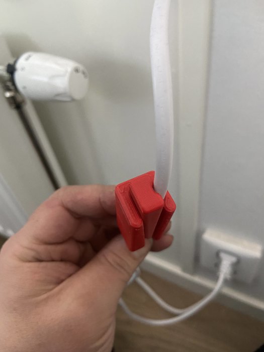 Hand håller en röd 3D-utskriven klämma med spiralvriden vit kabel för att demonstrera spiraliseringsteknik.