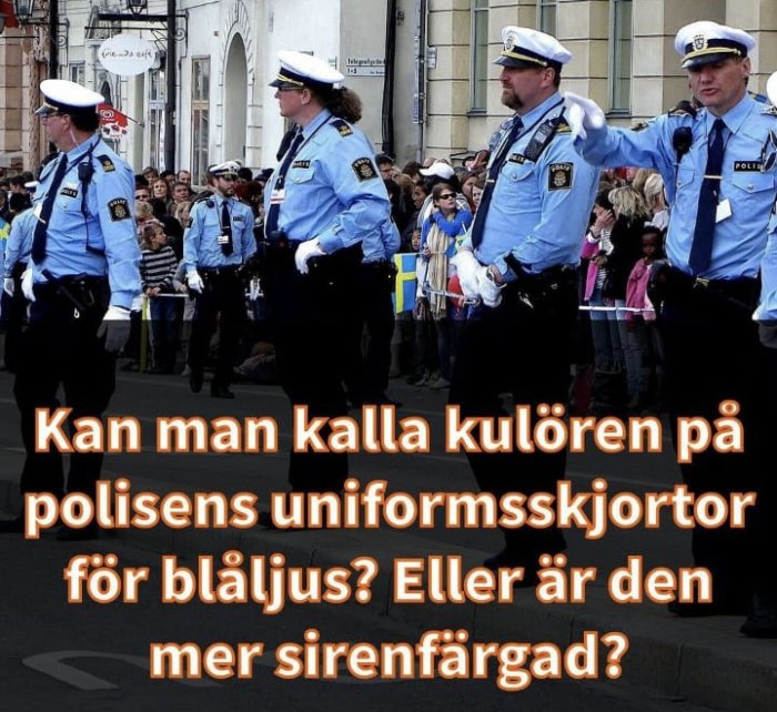 Poliser i uniform marscherar i en parad framför åskådare med text om färgen på deras skjortor.