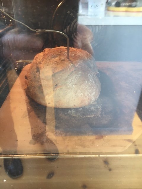 Ett bröd gräddas i ugnen, synligt genom en ugnslucka med reflektioner och skuggor.