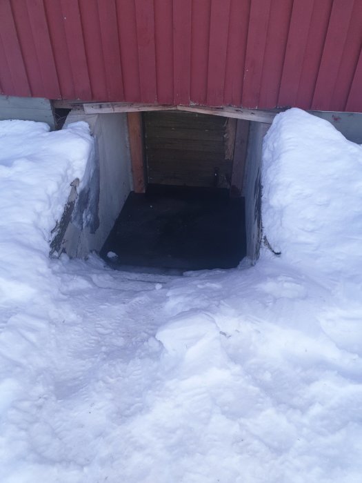 Översvämmad källaringång med is och snö utanför ett rött hus.