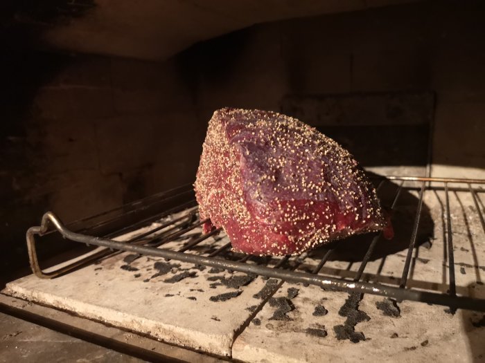 Älgpepparstek täckt med kryddor som steks i en ugn, sannolikt i en bakugn av täljsten.