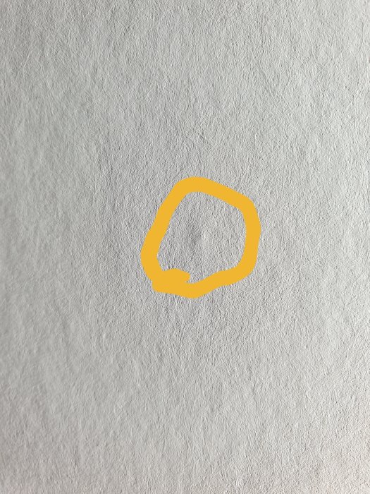 Klump under tapeten markerad med gul cirkel, vilket kan vara limrester eller bubbler.