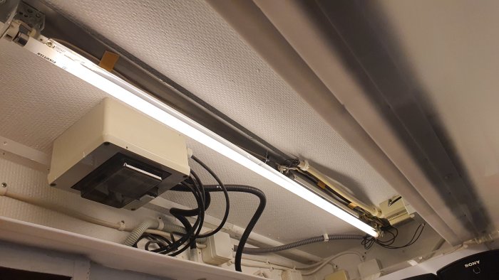 Tak klätt med opalskivor, ljudisolering och vitmålade balkar, samt elektronik och kablar.