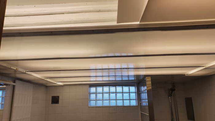 Renoverat badrum med höjt tak och opalskivor för ljusdiffusion, ljust och rymligt intryck.