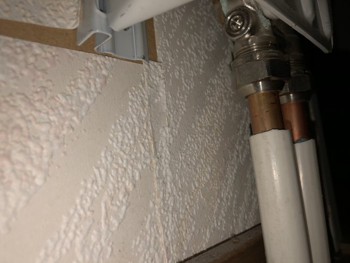 Närbild på termostat och rörledningar i en vägg som är del av ett 1-rörssystem för uppvärmning.