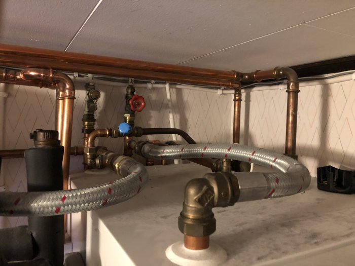 Värmesystem med kopparledningar, ventiler och insexskruv under en trappa, som avses att justera för likformig uppvärmning av huset.