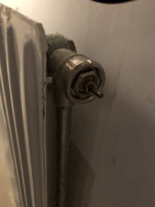 Termostat på ett element utan ratt, visar inre mekanism och anslutningsrör i ett hem.