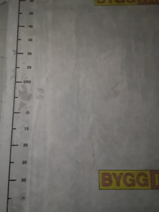 Close-up bild av en vägg med mätsticka och texten "BYGGI" synlig, vilket antyder ett bygg- eller renoveringsprojekt.