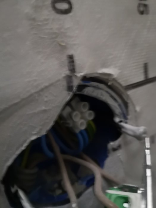 Otydlig bild av öppen elinstallation bakom vägg med synliga kablar och isolering.