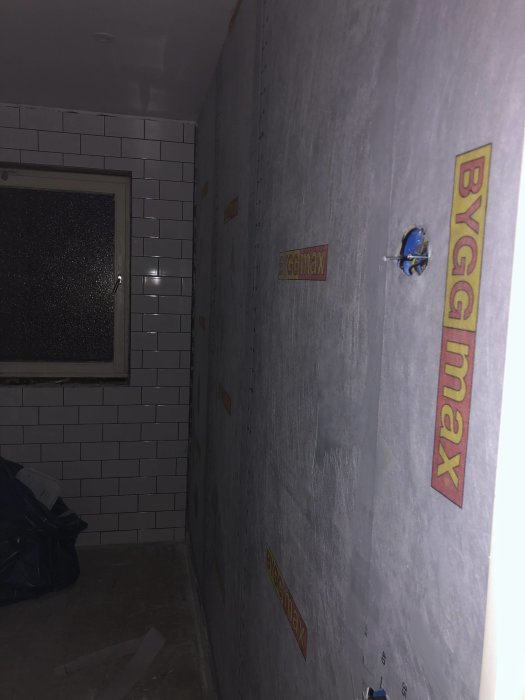 Renoveringsarbete med delvis kaklad vägg och nyinstallerad gipsvägg redo för kakling.