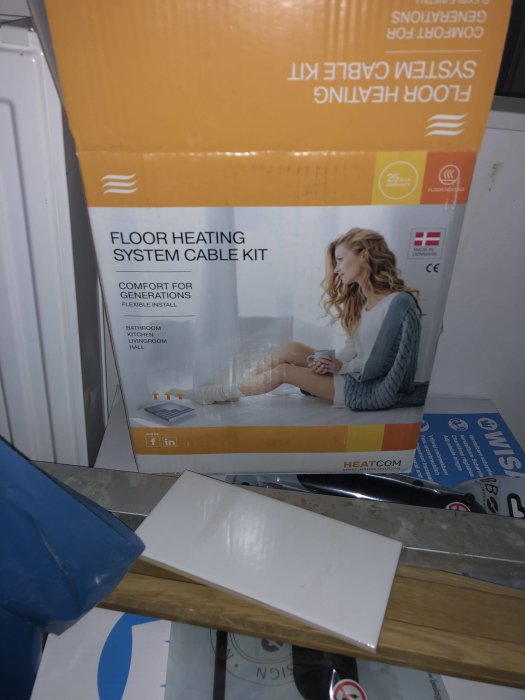 Packaged floor heating system cable kit and loose white tiles on a construction site.