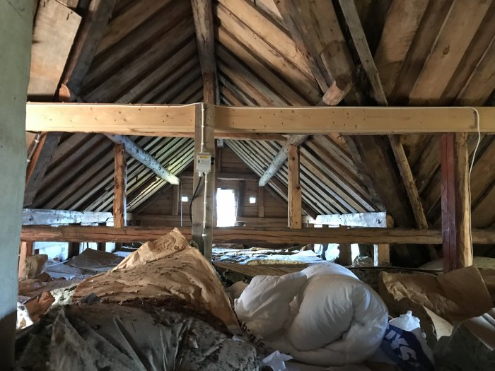 Inredning av ett vindrum med träbjälkar och synliga sparrar samt isoleringsmaterial på golvet.