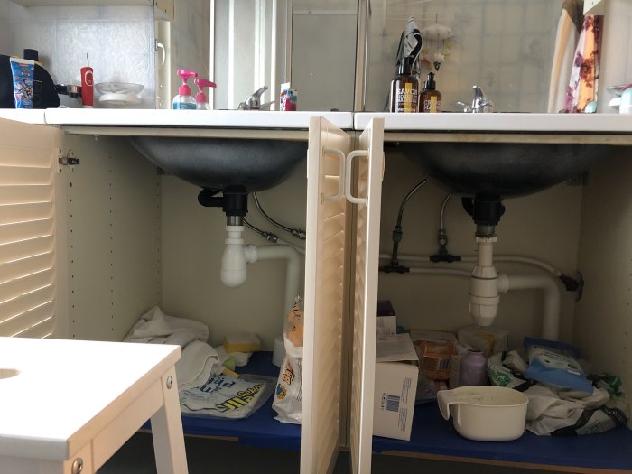 Under-sink view showing plumbing setup with T-connections for double sink, potential toilet water line.
