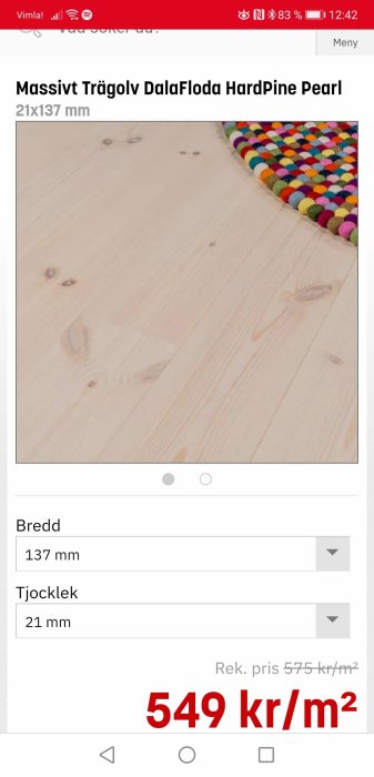 Närbild på massivt furugolv Dalaflo med synliga ådringar bredvid en färgglad mattkant på en online produktannons.
