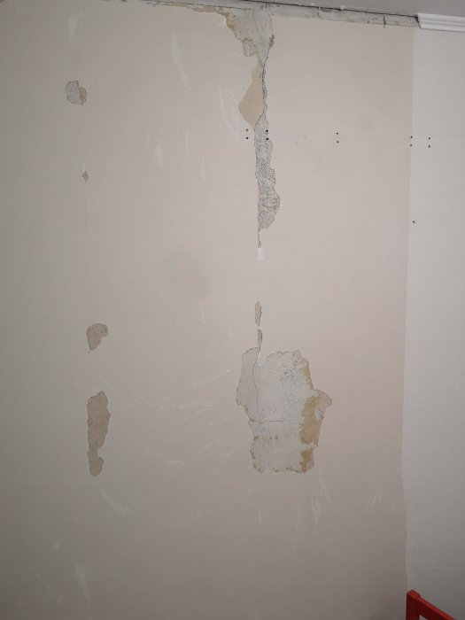 Vägg under renovering med tapetrester och synlig spricka där ny spackling planeras.