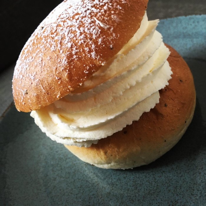 En semla med fluffig grädde och lock pudrat med florsocker på en tallrik.