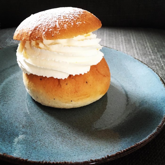 En traditionell svensk semla med vispad grädde på ett blått fat, pudrad med florsocker.