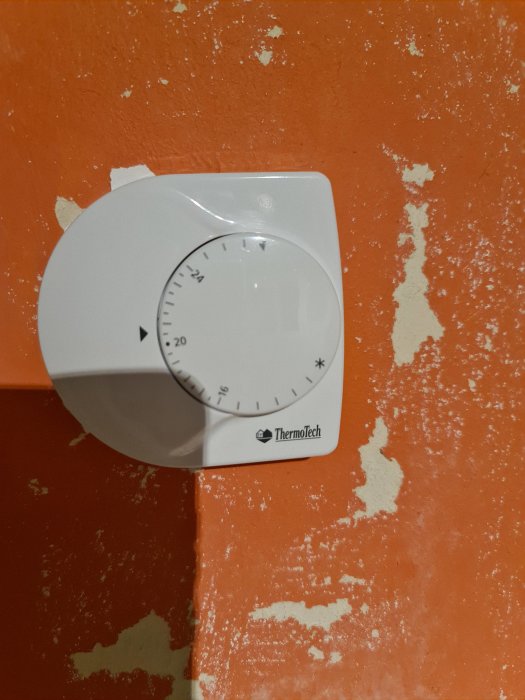 Vit Thermotech termostat monterad på en orange vägg med avflagande färg.