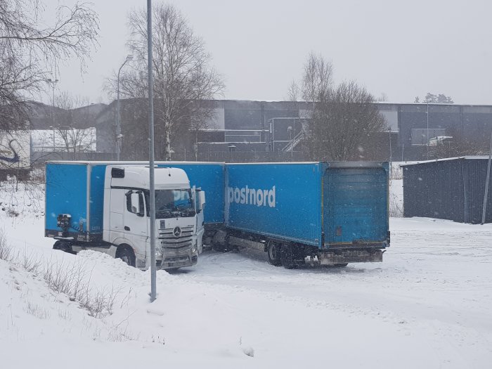 Lastbil fast i snön med texten "Postnord" på sidan under ett snöfall.