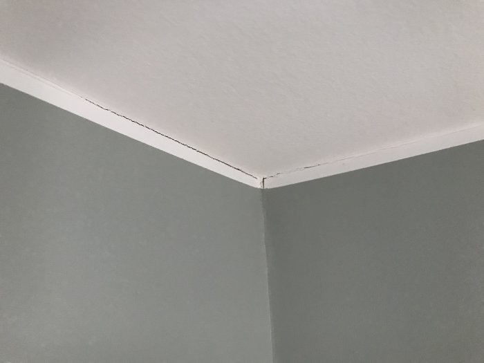Sprickor längs med hörnet av en nybyggd och målad rumsvägg nära taket.