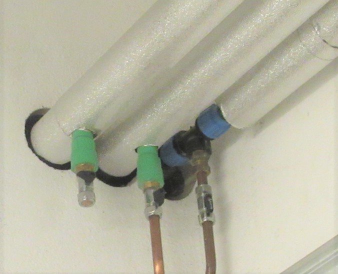 Kopparrör anslutna till isolerade plaströr genom kopplingar i ett VVS-installationssystem.