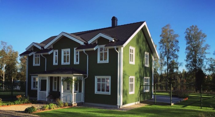 Ett stort grönt hus med vita knutar och en blå himmel i bakgrunden.
