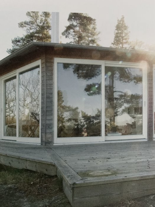 Lusthus med trädäck i skogsmiljö, tydliga tecken på förfall på trädäcket syns.