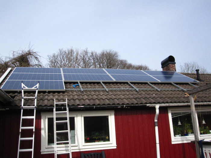 Solpaneler monterade ovanpå betongpannetaket på ett rött hus.