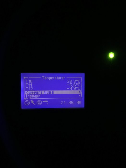 LCD-display som visar temperaturer och menyval i mörker med en diffus grön bakgrundsbelysning.