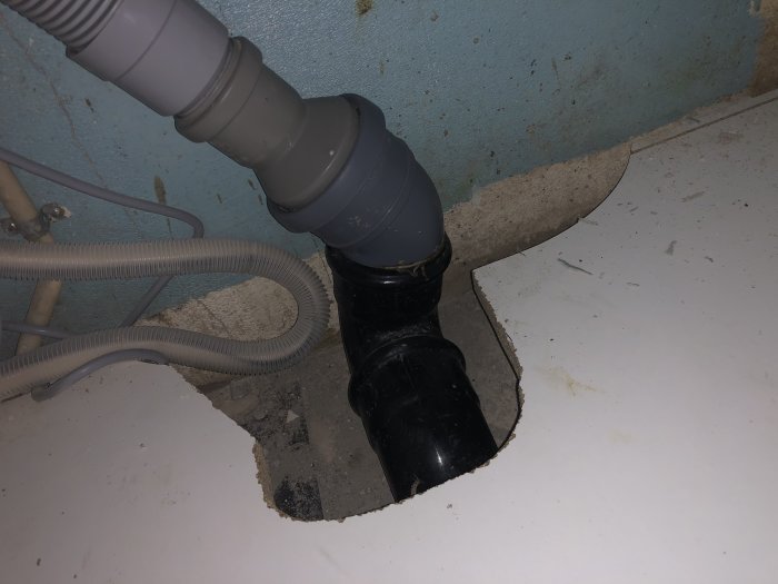 Nyinstallerat avloppsrör i kök med bortskuren plastmatta och synliga rör.