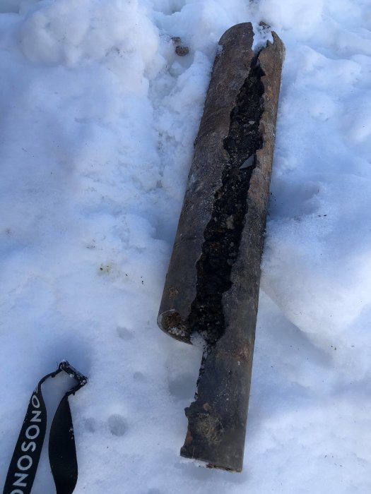 Del av sönderrostat gjutjärnsrör på snötäckt mark, visar omfattande rostskador och hålighet.