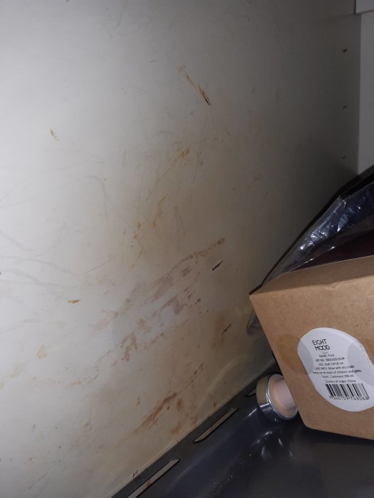 Fläckar i olika nyanser av brunt och orange på insidan av ett öppet köksskåp, eventuellt mögel eller smuts.