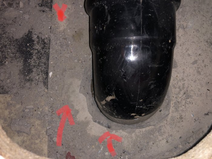 Plaströr från köksavlopp som går ner i betonggolv, med röda markeringar som indikerar spackel.