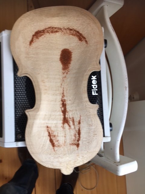 En rå träviolinbotten med spårmönster av paprikapulver, placerad på ett bord bredvid en stol.