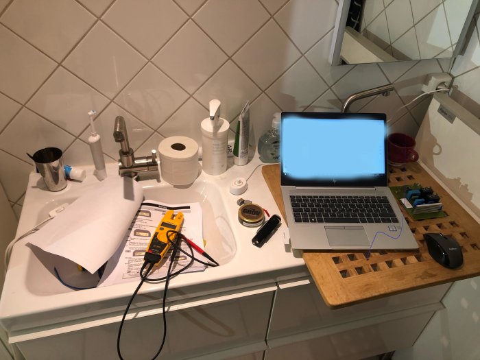Arbetsplats hemma med multimeter, laptop och diagram på handfatet för felsökning av NIBE Fighter 1215-5 värmepump.