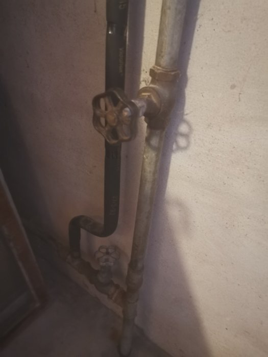 Gamla rörinstallationer med ventiler mot en betongvägg i en källare.