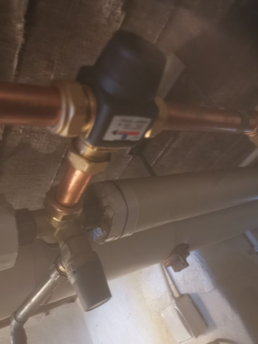 Otydligt fotograferad bild på röranslutningar och ett ventilkopplingsstycke vid en pump i ett garage.