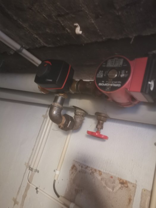 Installationsrör och en pumpkoppling med en röd spärrventil på en vägg i ett garage.