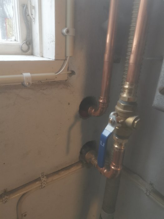 Rörinstallation med kopparledningar och en blå ventil i ett garage nära pumpen.