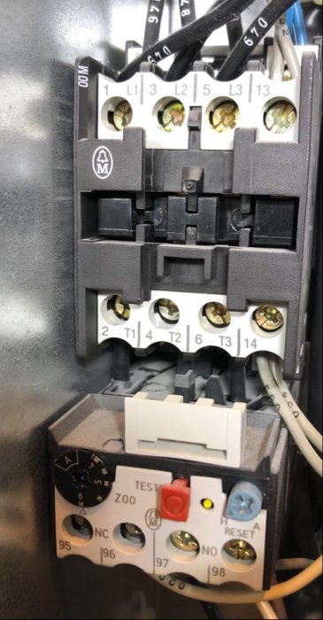 Öppen elektrisk kretsbrytare med tydligt markerade kablar och inställningsknappar på en komponent i värmepumpssystemet.